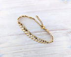 A gold-toned beaded chain bracelet with alternating white and gold square beads, displayed on a light-colored wooden surface.