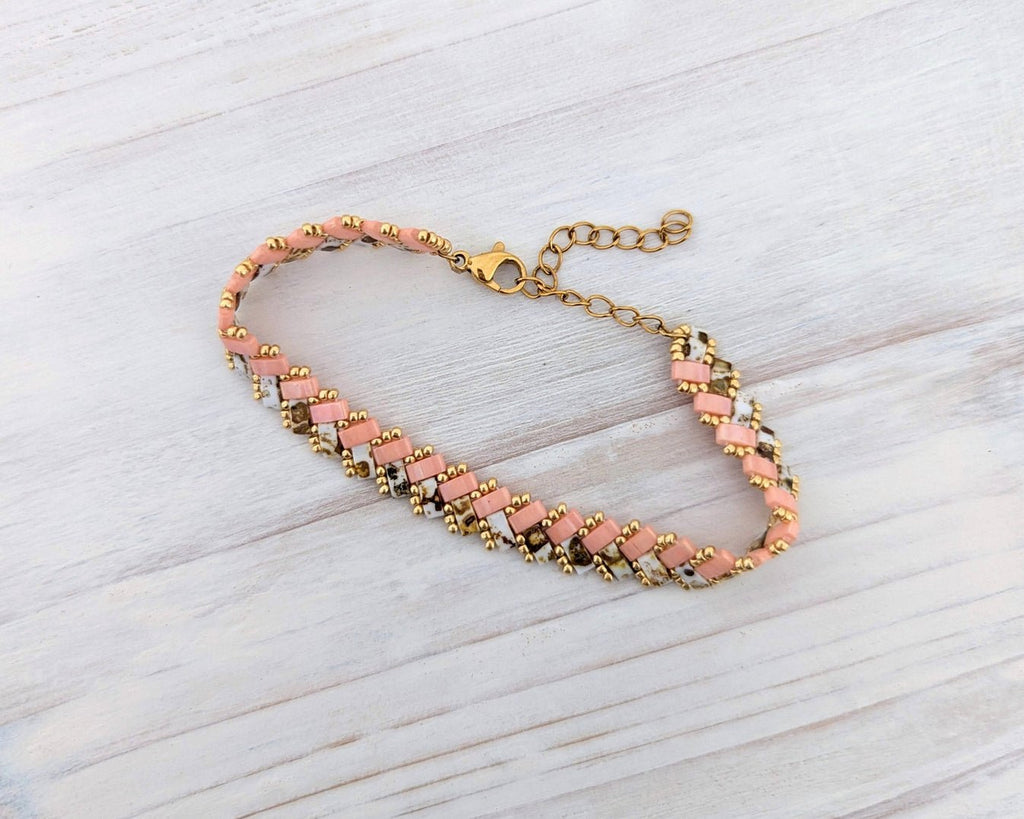A handmade beaded bracelet with pink and white beads, gold spacer beads, and a gold clasp, displayed on a light gray wood background.