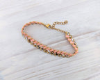 A handmade beaded bracelet with pink and white beads, gold spacer beads, and a gold clasp, displayed on a light gray wood background.