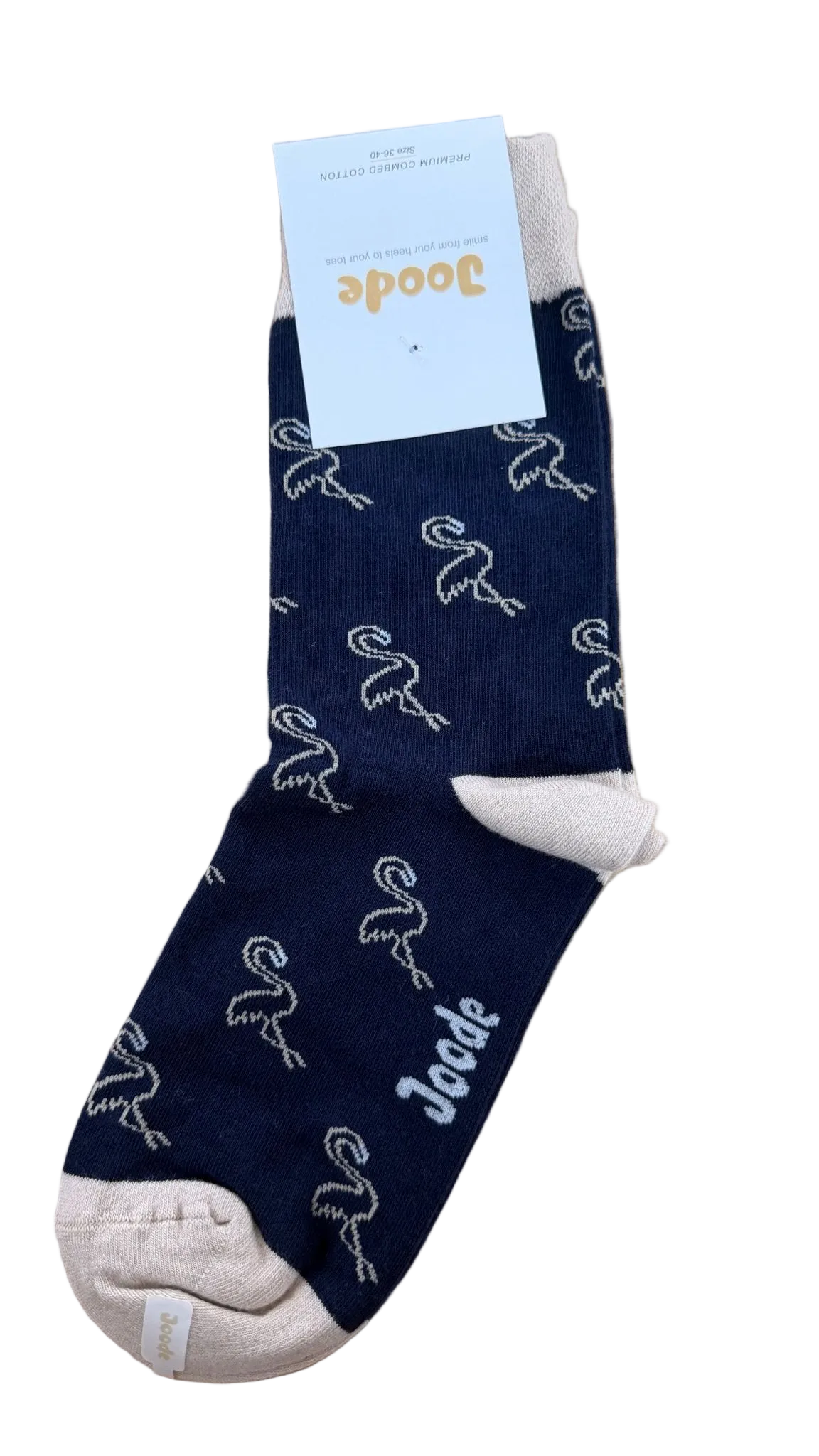 A single navy blue sock with a white flamingo pattern and a white cuff, shown on a light wood background with a white paper tag attached. The brand name 'Joode' is visible on the tag and printed on the sock.