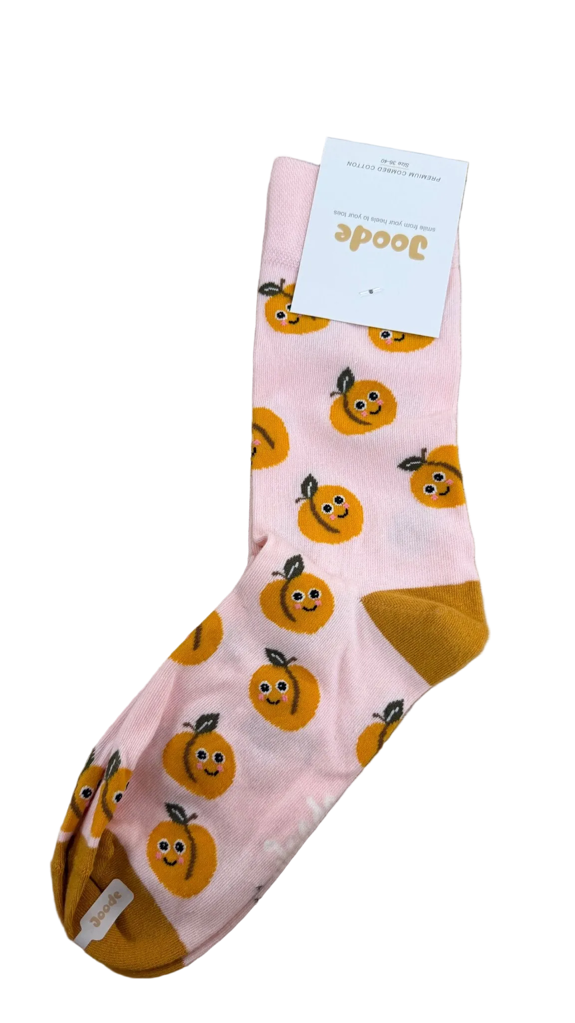 A single pink crew sock with a pattern of smiling orange pumpkins, featuring mustard yellow heels and toes, laid flat on a light wood surface with its white retail tag attached.