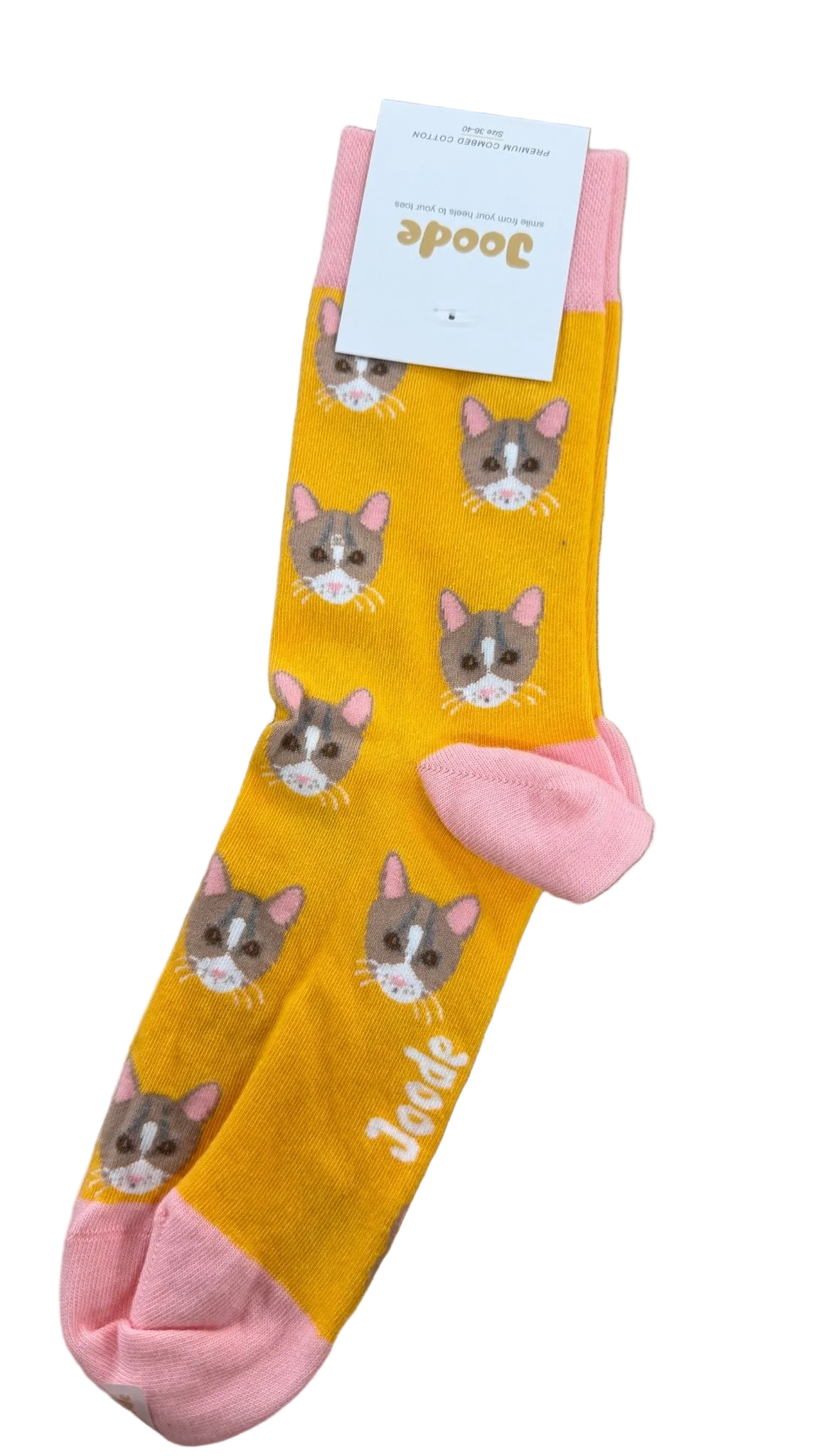 A pair of yellow socks with pink toes and heels, featuring a repeating pattern of gray and white cat faces, laid flat on a wooden surface. A white paper tag with the brand name 'Jodis' is attached at the top.