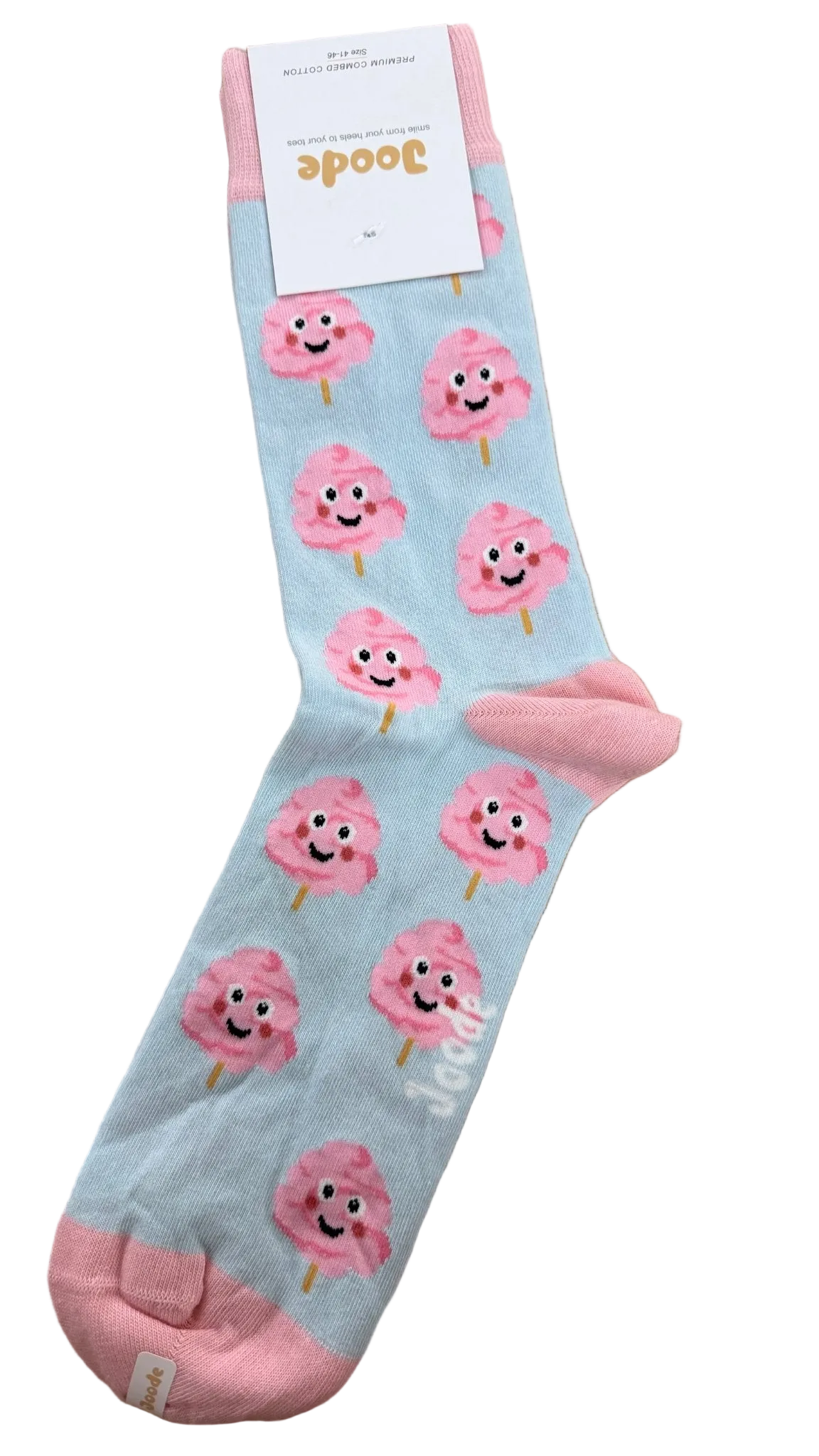 A single light blue sock with pink toes, heels, and cuffs, decorated with a repeating pattern of smiling pink cotton candy characters. The sock is laid flat on a wooden floor, with its white paper brand tag visible at the top.