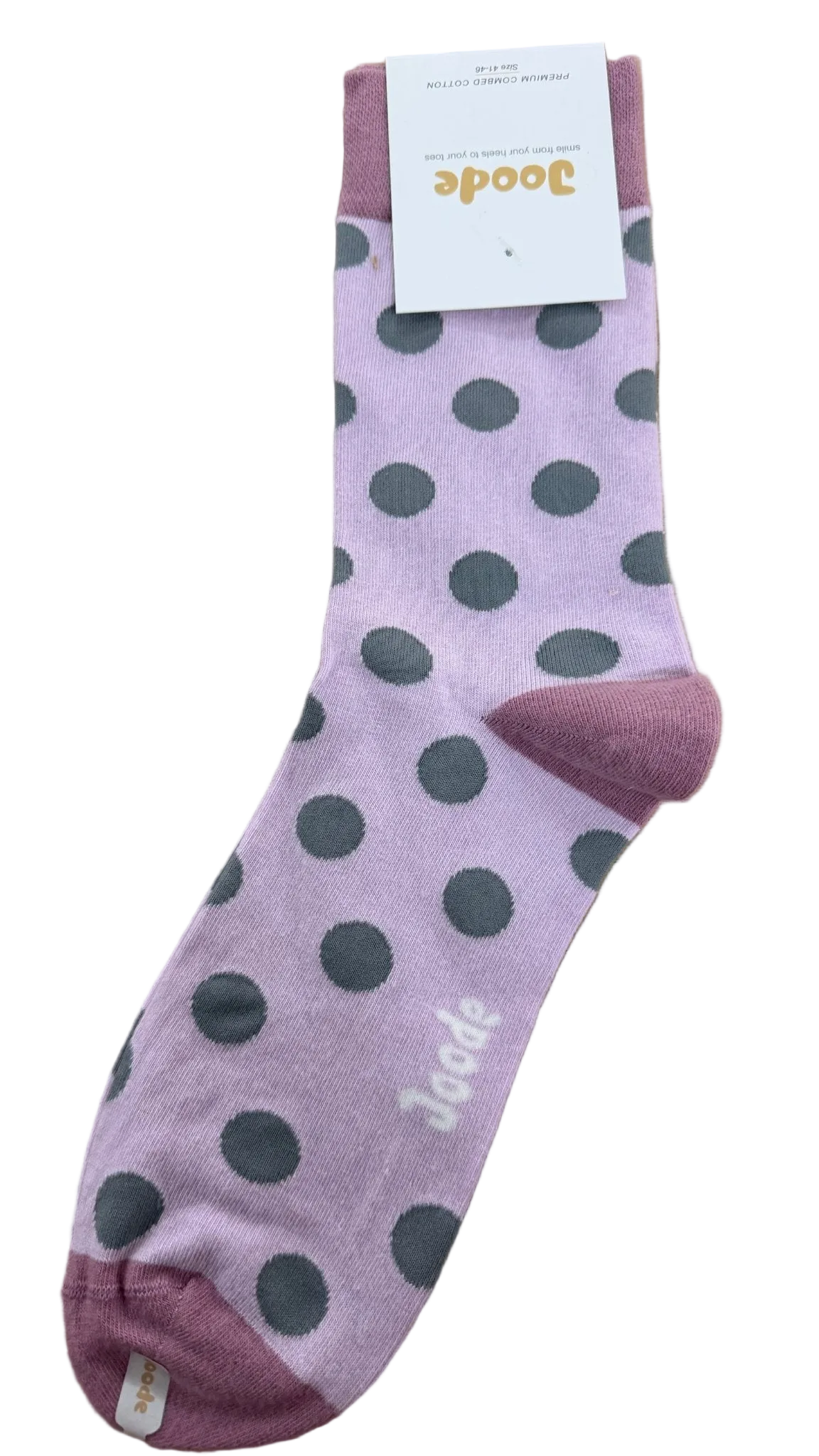 A single pinkish-purple sock with large dark gray polka dots, a matching pink heel and toe, and a white paper tag attached near the cuff, photographed on a wooden surface.