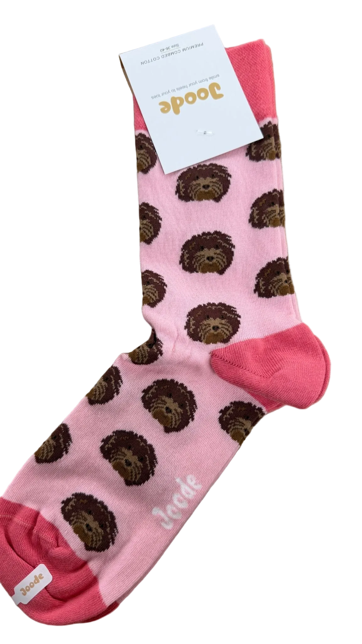 A single pink crew sock with a repeating brown dog print and bright pink toe, heel, and cuff, laid flat on a wood surface with a white Doode brand tag attached.