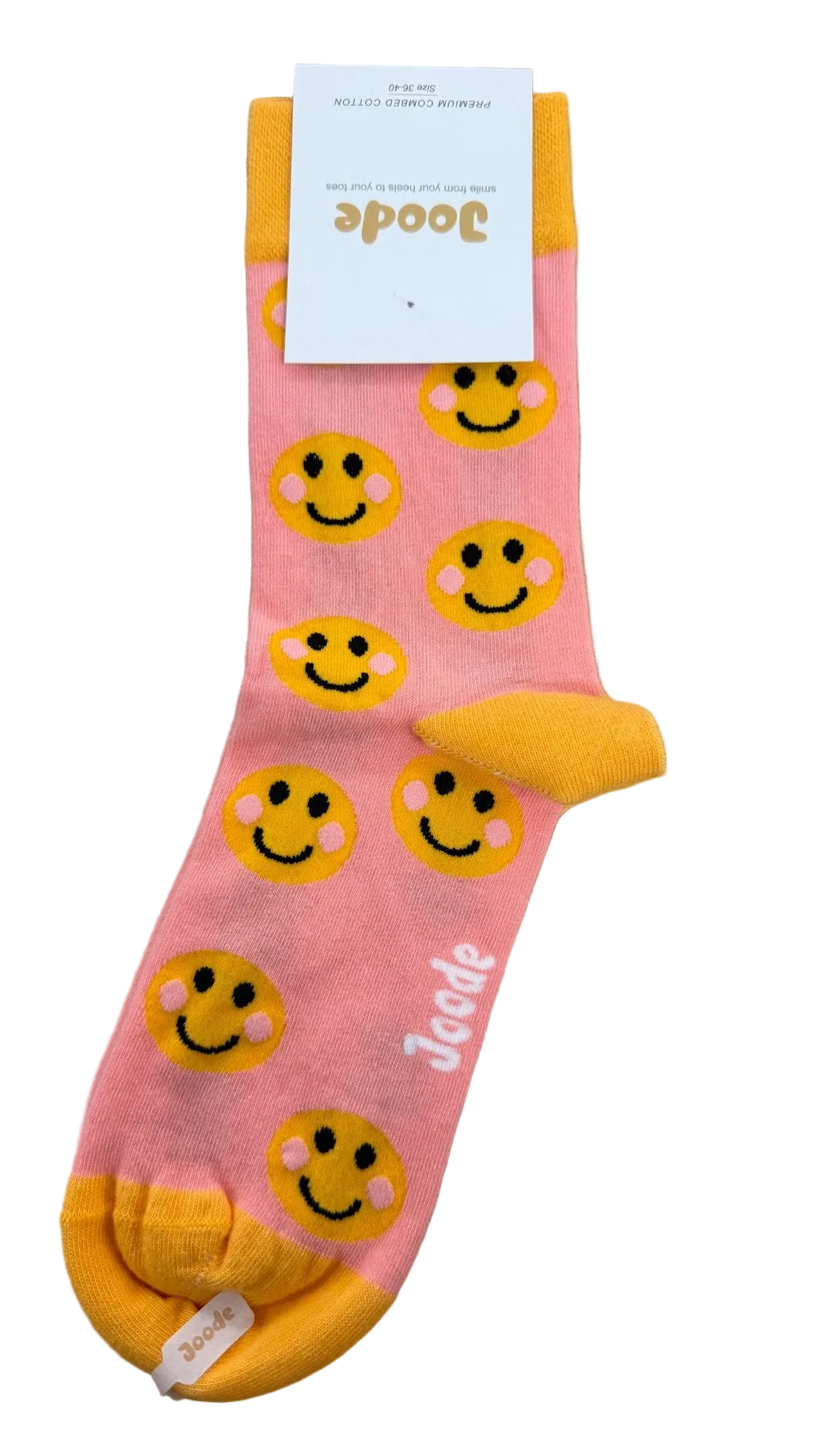 A single pink crew sock with a yellow toe, heel, and cuff, decorated with a repeating pattern of yellow smiley faces. The brand name 'Joode' is printed in white script near the foot, and the product is displayed on a light wood background with its retail tag attached.