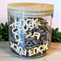 Jar filled with wooden letters spelling 'FUCK' on a light surface.