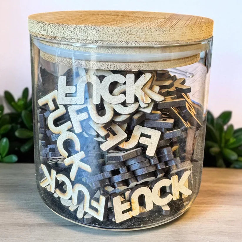 Jar filled with wooden letters spelling 'FUCK' on a light surface.