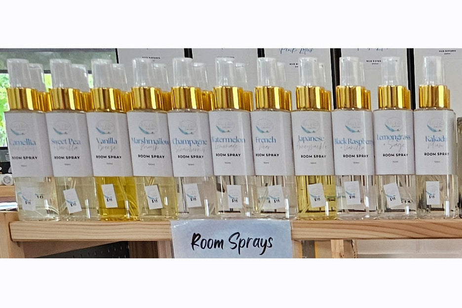 Row of white bottles with gold caps labeled 'Room Sprays' on a white background.