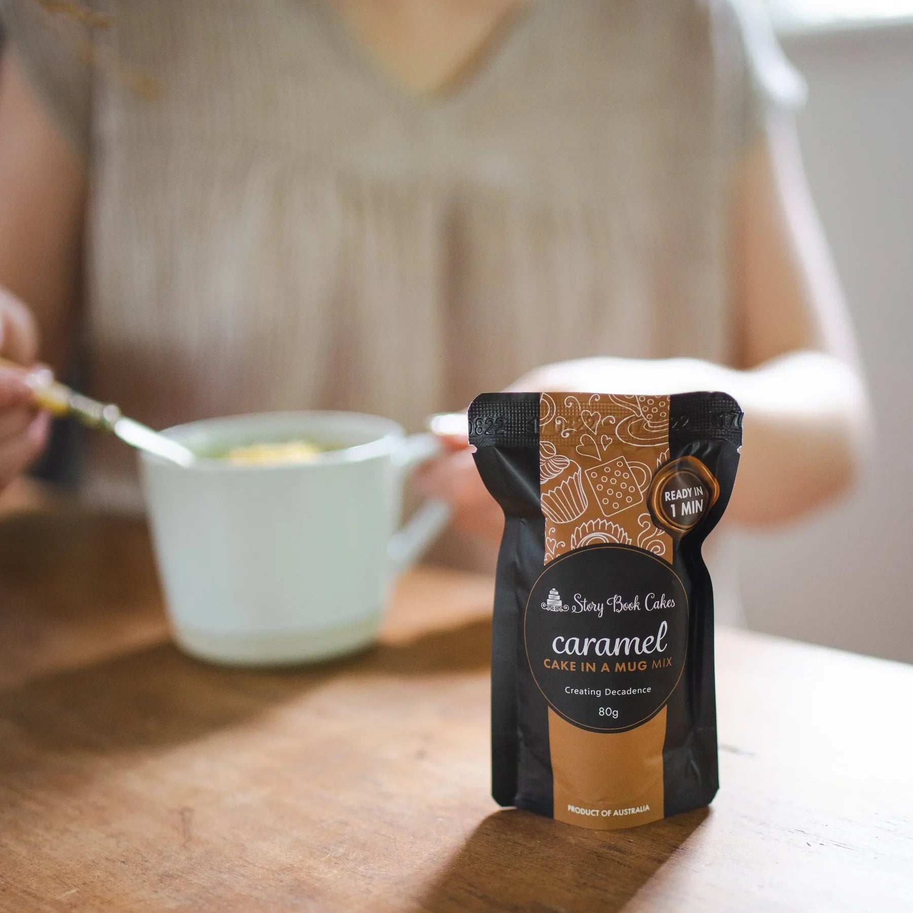 Person holding a spoon over a bowl with a container of coffee on a wooden table.