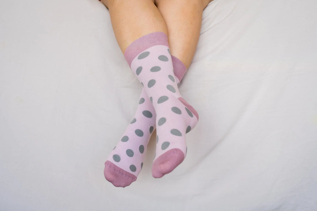 Pink socks with gray polka dots worn by a person on a light background
