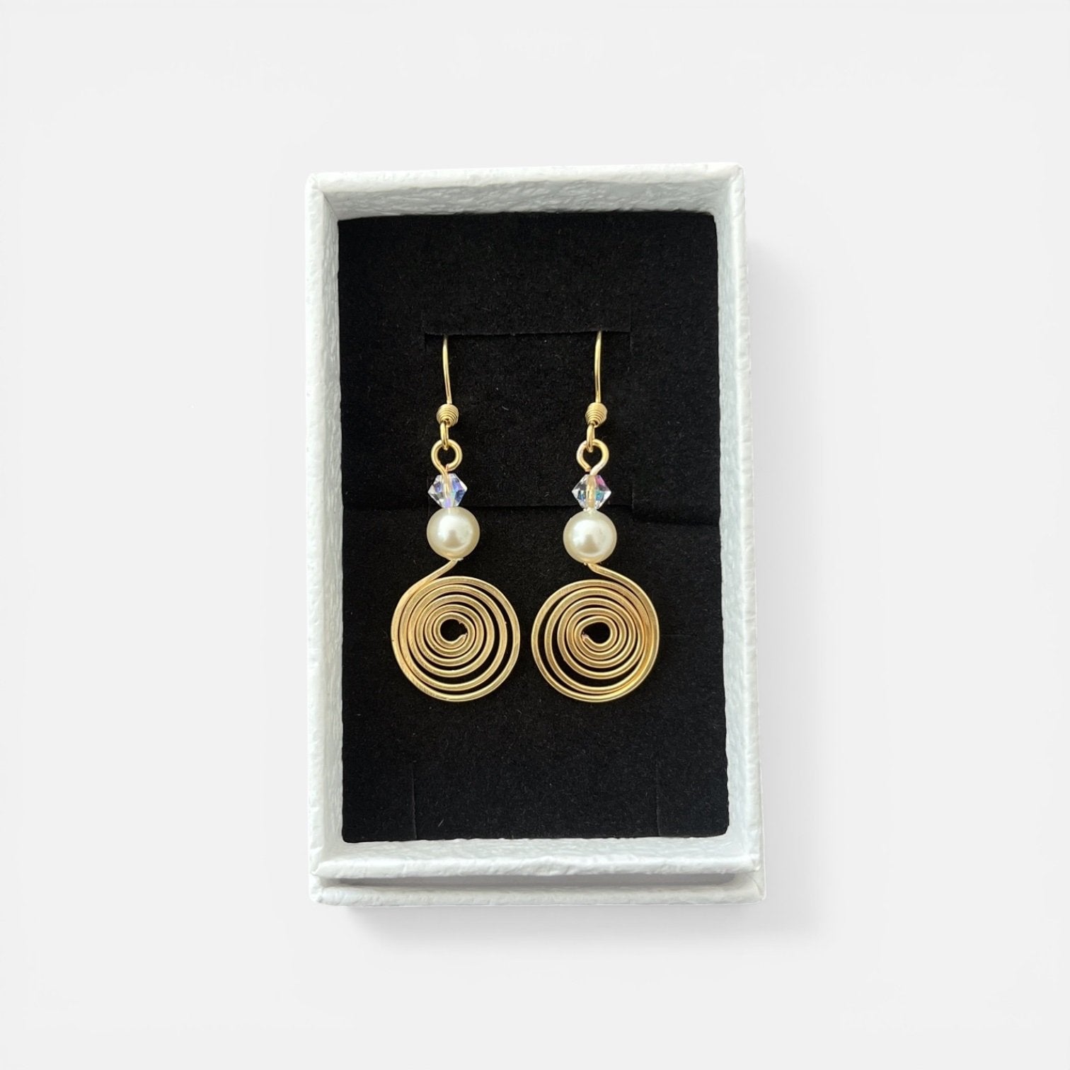 Gold spiral earrings with pearls and crystals in a black jewelry box on a white background